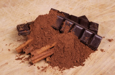 chocolate bars with cinnamon sticks and pile cocoa powder on wooden chopping board