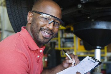 Portrait of a happy African American male mechanic writing notes in garage