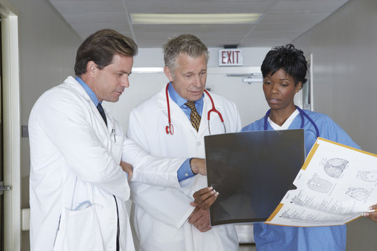 Team of three multiethnic doctors analyzing x-ray report in hospital corridor