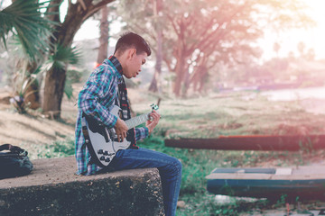 Fototapeta premium Handsome young man playing guitar in the riverside, enjoy playing guitar.