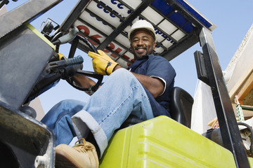 Low angle view of a happy African American industrial worker driving forklift