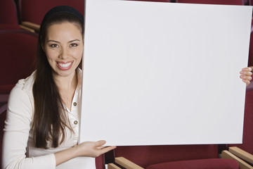 Portrait of a mixed race businesswoman holding blank placard while sitting in auditorium