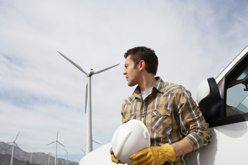 Male engineer holding hardhat by car at wind farm