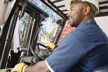 Happy African American industrial worker driving forklift at workplace