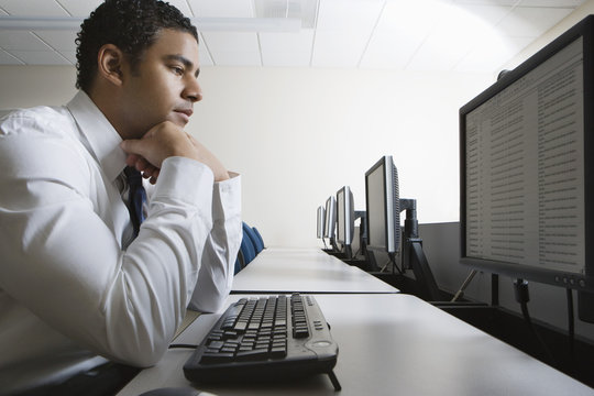 Side view of businessman with hand on chin looking intently at screen while sitting in computer lab