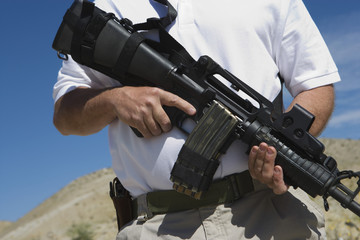 Midsection of a man holding machine gun at firing range
