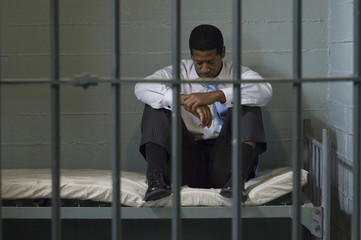 Businessman sitting on bed in prison cell