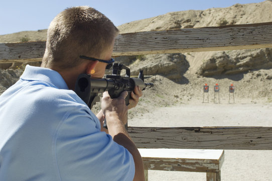 Rear view of a man aiming machine gun at firing range during weapons training