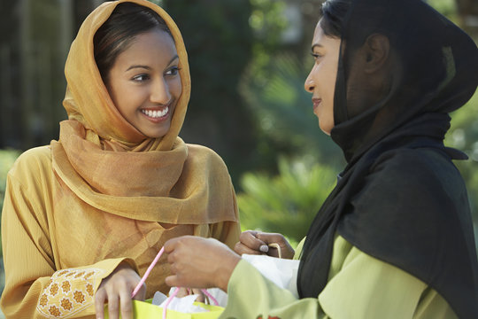 Two happy young Asian Muslim women in traditional wear talking outdoors