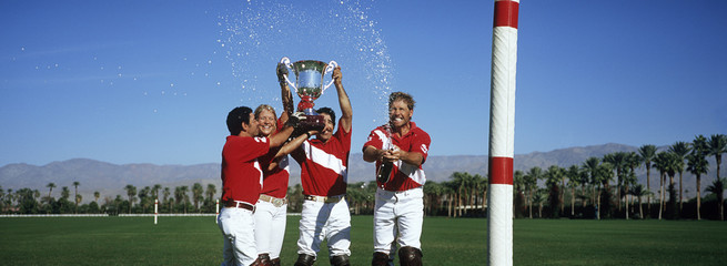 Happy multiethnic polo team celebrating with trophy on field