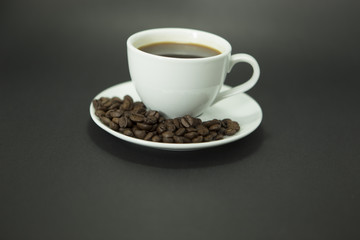 Coffee cup and coffee beans on dark background.
