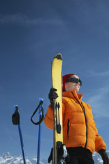 Naklejka premium Low angle view of happy woman in winter jacket holding ski against blue sky