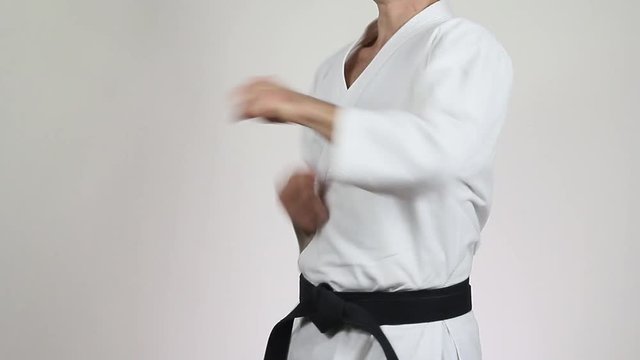 With a black belt in white kimono sportsman makes a punch on a gray background