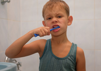 Мальчик семи лет чистит зубы щеткой перед сном в ванной комнате  - obrazy, fototapety, plakaty