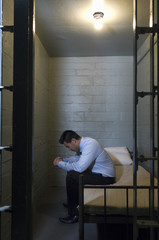 Upset young businessman sitting on bed in prison