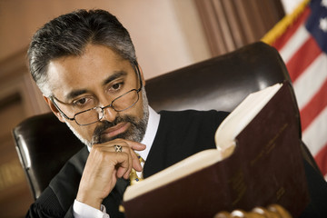 Male judge reading law book for reference in courtroom