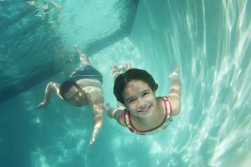 Happy elementary girl with father swimming underwater in pool