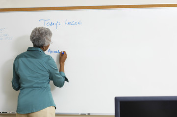 Rear view of a senior teacher writing on the whiteboard in classroom - Powered by Adobe
