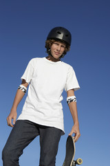 Low angle view of teenage skateboarder standing against blue sky