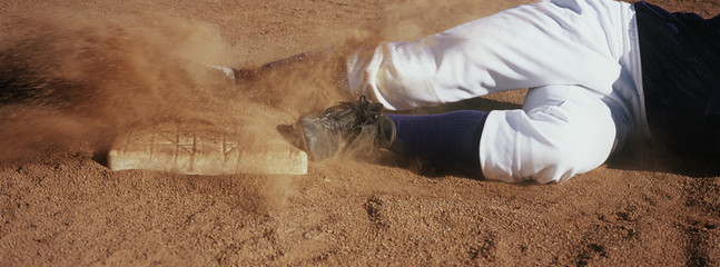 Low section of baseball player sliding towards base on field