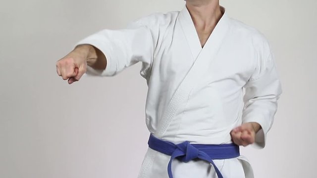 On a gray background athlete in a white kimono with a blue belt making punch