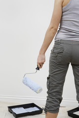 Midsection of a woman holding paint roller standing against white wall
