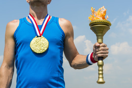 American gold medal athlete standing with sport torch in front of blue sky