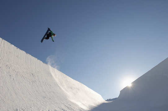 Low angle view of snowboarder performing stunts in park against blue sky on a sunny day