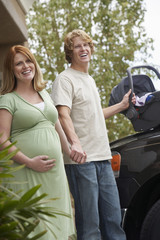 Portrait of an expectant young couple with baby carrier by car