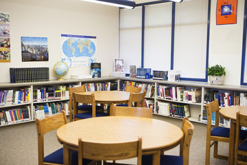 Tables and chairs with books arranged on shelves in high school library