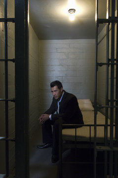 Depressed young businessman sitting on bed in prison