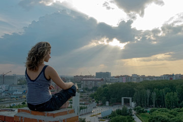 Fototapeta na wymiar Young attractive woman relaxes on edge of high building roof