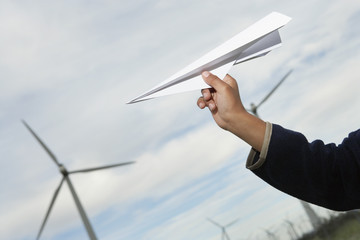 Little boy's hand throwing paper plane at wind farm