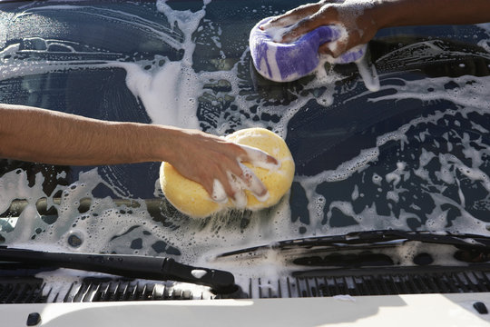 Closeup of hands washing car with sponges