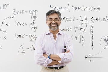 Portrait of a male lecturer standing with arms crossed against white board