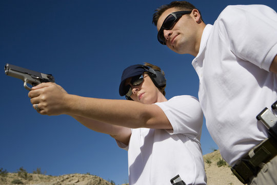 Low angle view of instructor assisting woman with hand gun at firing range
