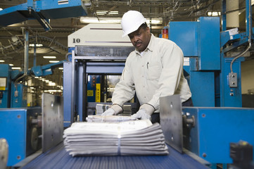 Side view of a man working on newspaper production line in newspaper factory