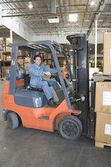 Portrait of a smiling man operating forklift truck in distribution warehouse