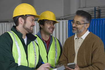 Multiethnic men discussing with clipboard and calculator in the factory