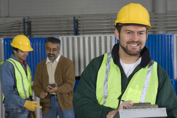 Smiling man in protective wear with colleague in background at factory 