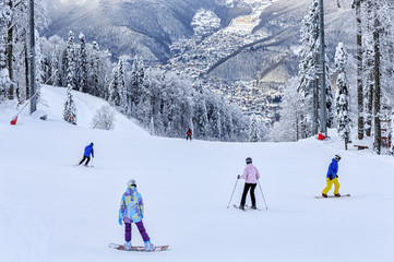 Skiers and snowboarders riding on a ski slope in Sochi mountain ski resort on snowy winter mountain background