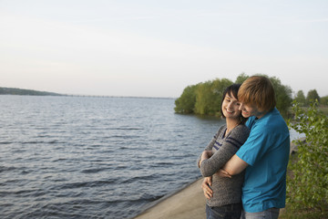 Fototapeta premium Side view of a smiling young couple embracing on lakeshore