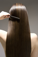 Closeup rear view of a woman combing her long brown hair against gray background