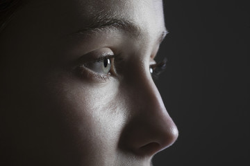 Closeup side view of a teenage girl looking away against black background