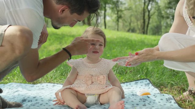 CLOSE UP: Sympathetic caring parents applying sunscreen on soft baby girl's skin