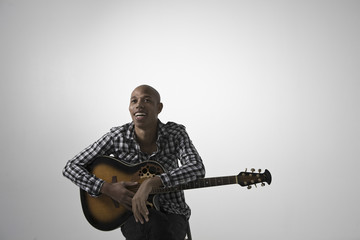 Portrait of a young happy man with guitar sitting against gray background