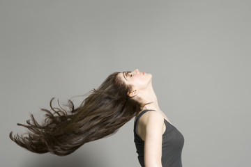 Side view of a woman with long brown hair blowing in wind against gray background