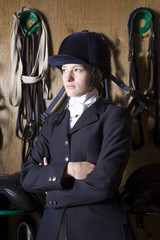 Thoughtful female horseback rider with reins hanging on wooden wall in background