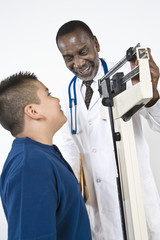 Happy male doctor checking boy's weight on weighing scale in clinic