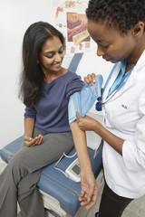 Female doctor checking happy Indian patient's blood pressure at the clinic
